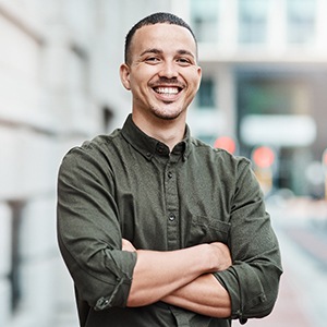 Man smiling with crossed arms outside