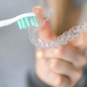 Patient using toothbrush to clean aligner