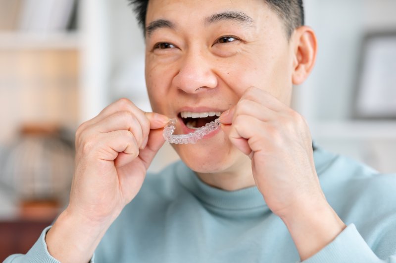 Man holding an Invisalign clear aligner near his mouth